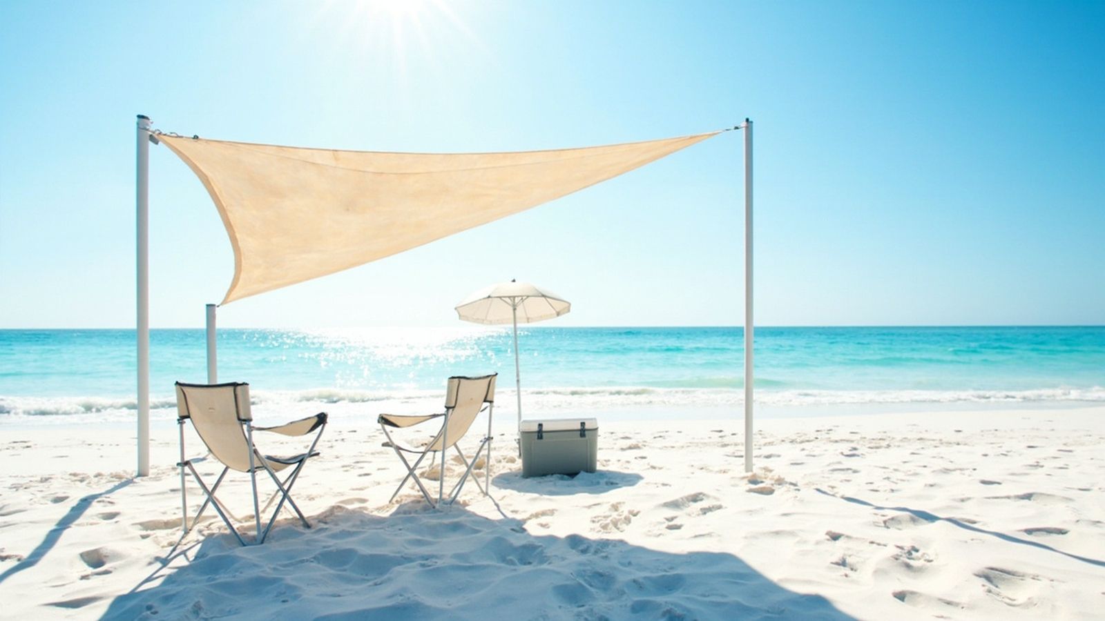 Open-top pole beach canopy over folding chairs and a cooler on bright sand